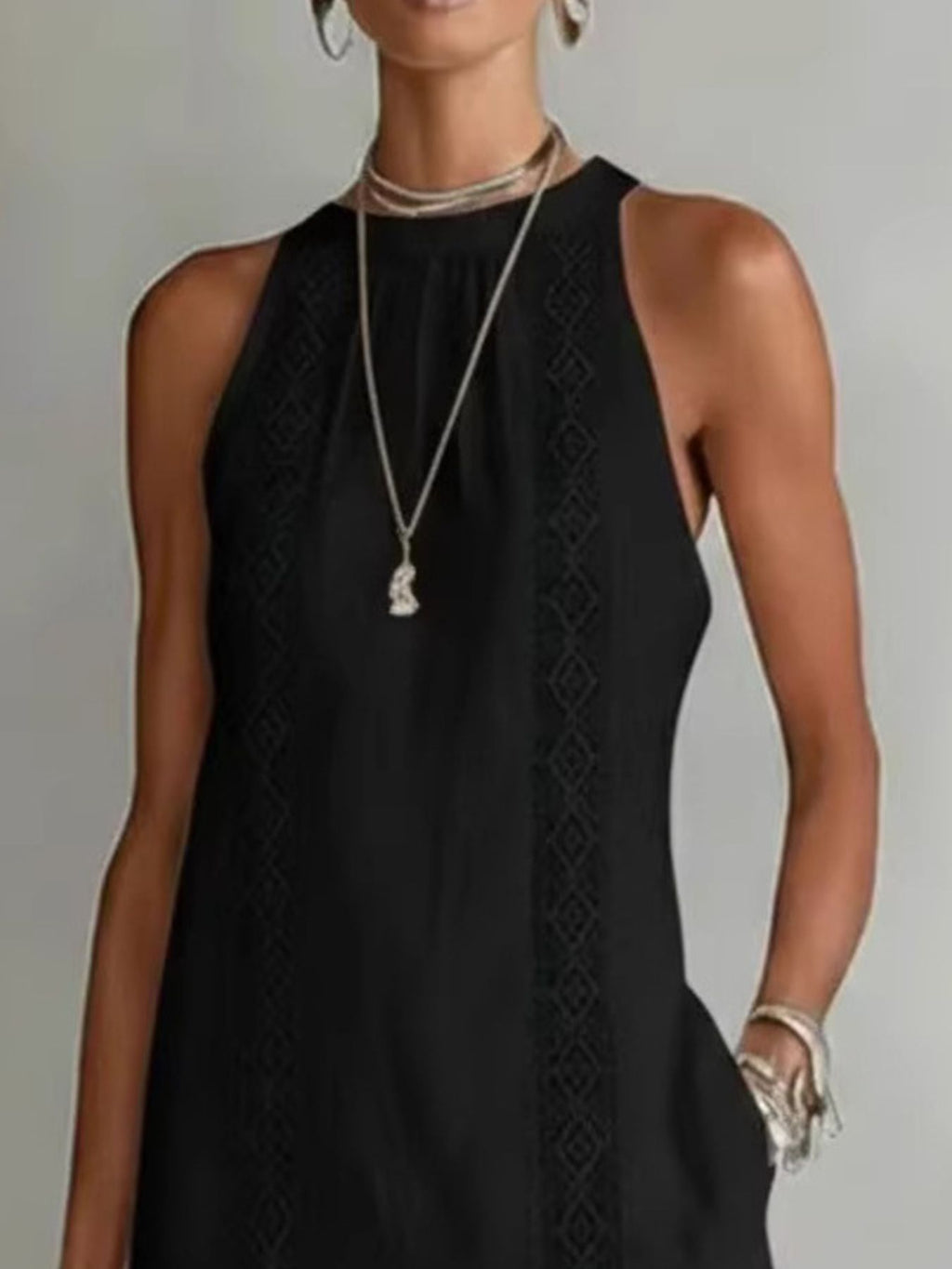 Woman wearing a black sleeveless dress with intricate detailing on a plain background