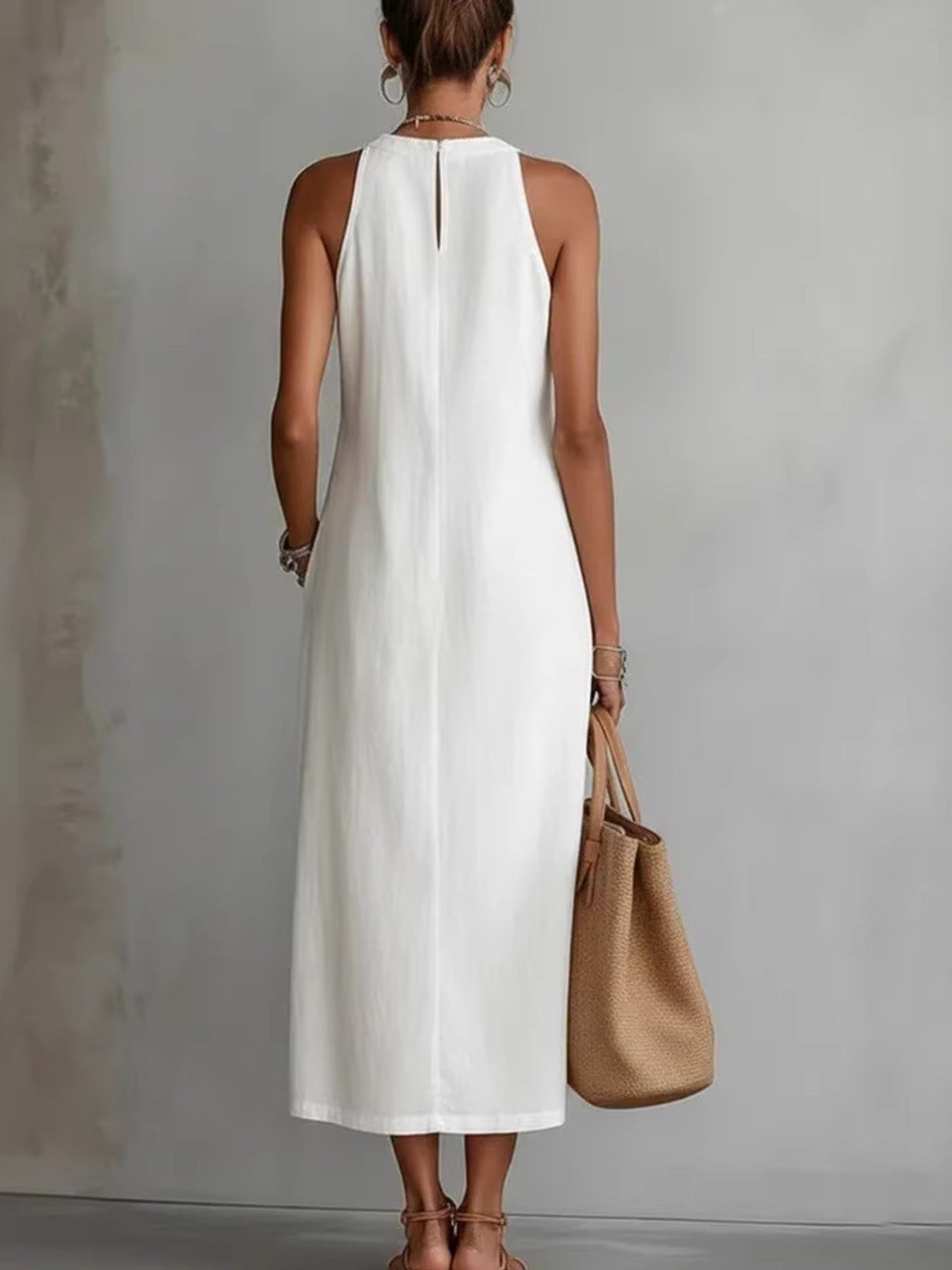 Woman wearing a white sleeveless dress holding a brown handbag against a gray background